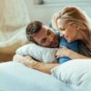 A couple lying close together in bed, talking and smiling in soft morning light