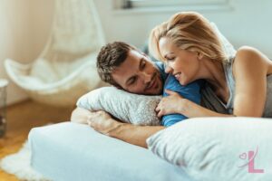 A couple lying close together in bed, talking and smiling in soft morning light