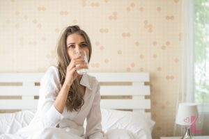 Woman drinking a glass of water in bed on a calm morning