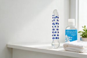 Clear textured glass dildo beside a bottle of water-based lubricant on a bathroom shelf