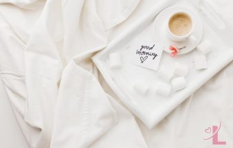 Breakfast tray with a cup of tea on soft white bedding in morning light