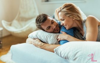 A couple lying close together in bed, talking and smiling in soft morning light