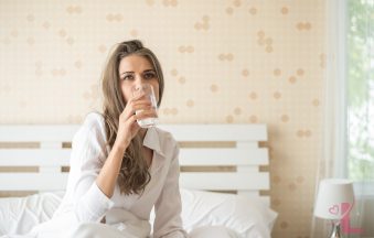 Woman drinking a glass of water in bed on a calm morning
